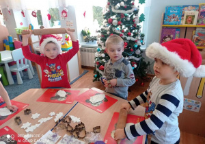 Dzieci z rozwałkowanej masy wycinają foremkami świąteczne kształty (choinki, gwiazdki, reniferki itp.)